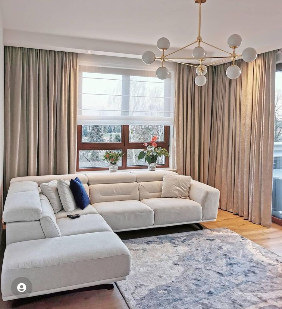 salon z beżowymi zasłonami i roletą rzymską białą